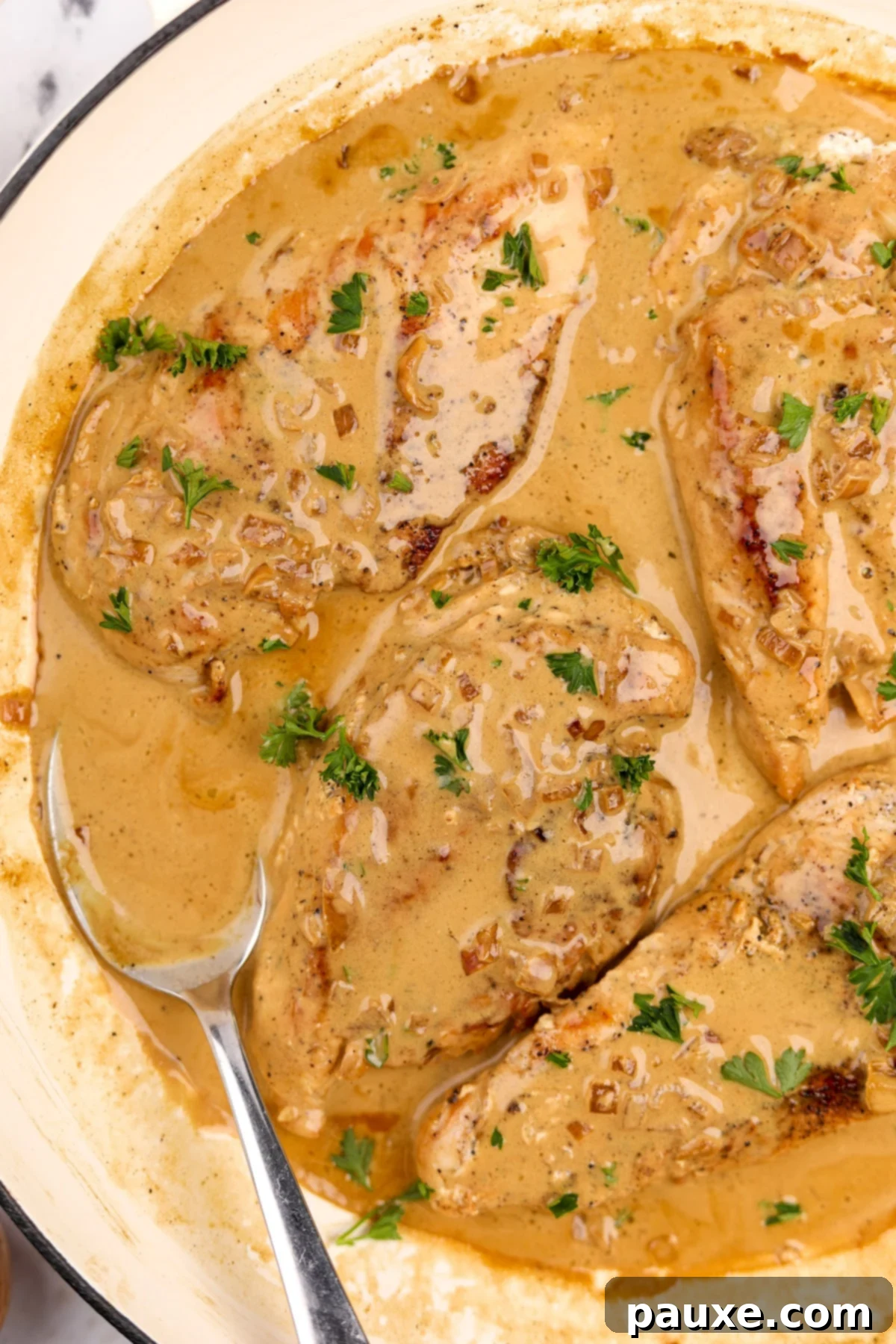 Four golden-brown chicken breasts resting in a rich, creamy Diane sauce, with a small spoon showcasing the sauce on the side.