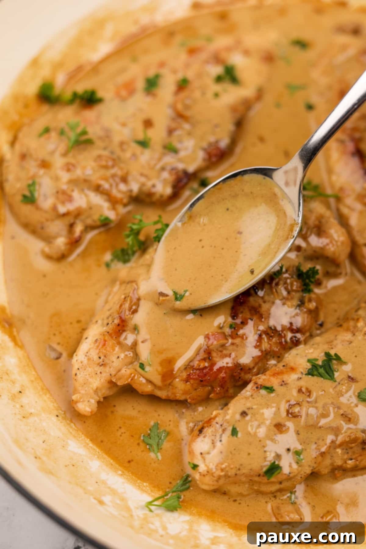 A close-up shot of a hand spooning the creamy Diane sauce over a piece of cooked chicken breast in the skillet, showcasing the rich texture.