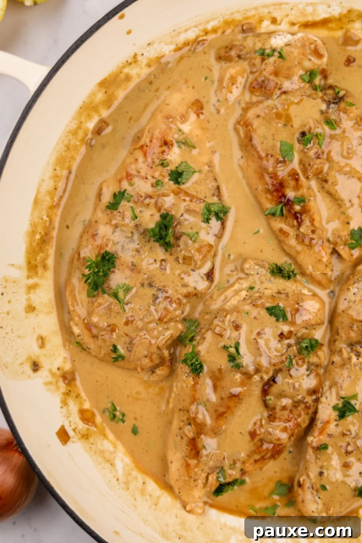 A beautiful coated cast iron skillet featuring creamy chicken breasts, generously garnished with fresh parsley, presented as a finished dish.