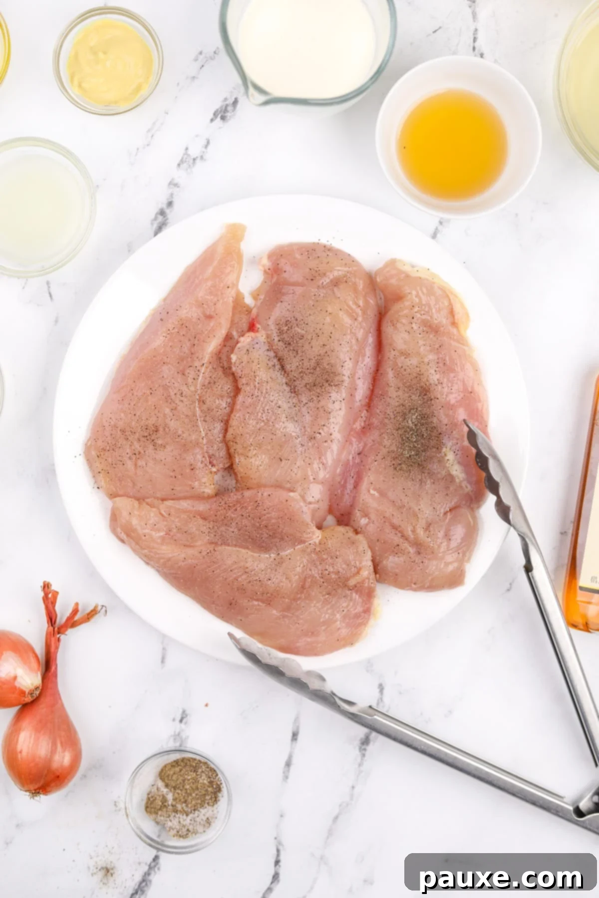 A white plate with chicken cutlets seasoned generously with salt and black pepper.