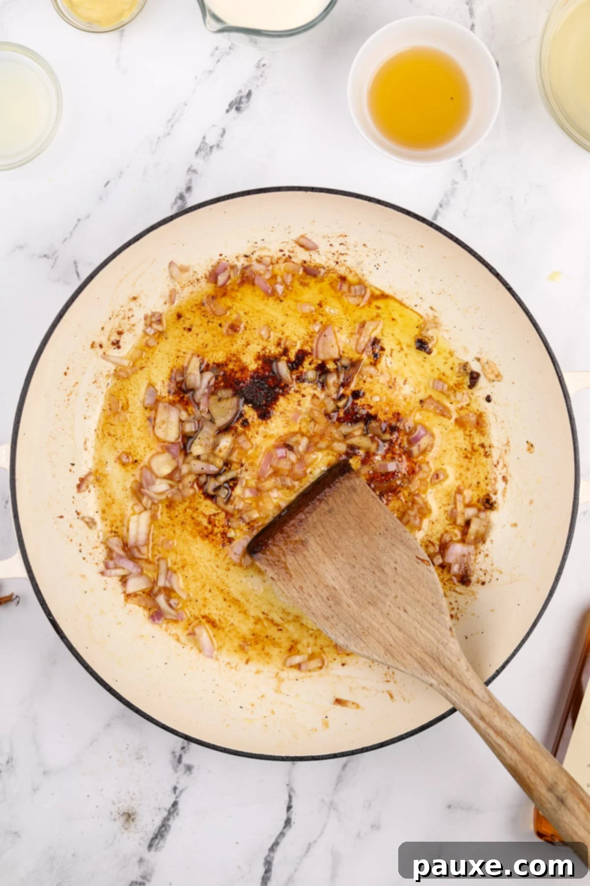 Minced shallot being sautéed in a skillet with the remaining oil and butter, softening to release its aroma.
