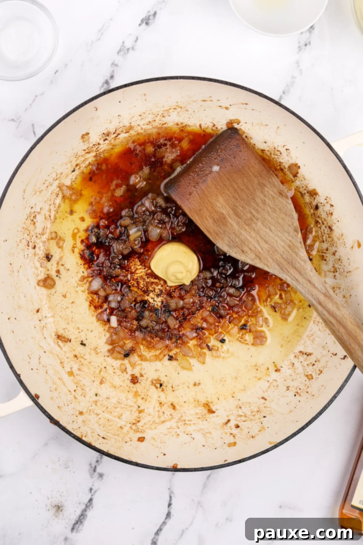 Dijon mustard, brandy, and lemon juice being added to the skillet with sautéed shallots, ready to form the base of the pan sauce.