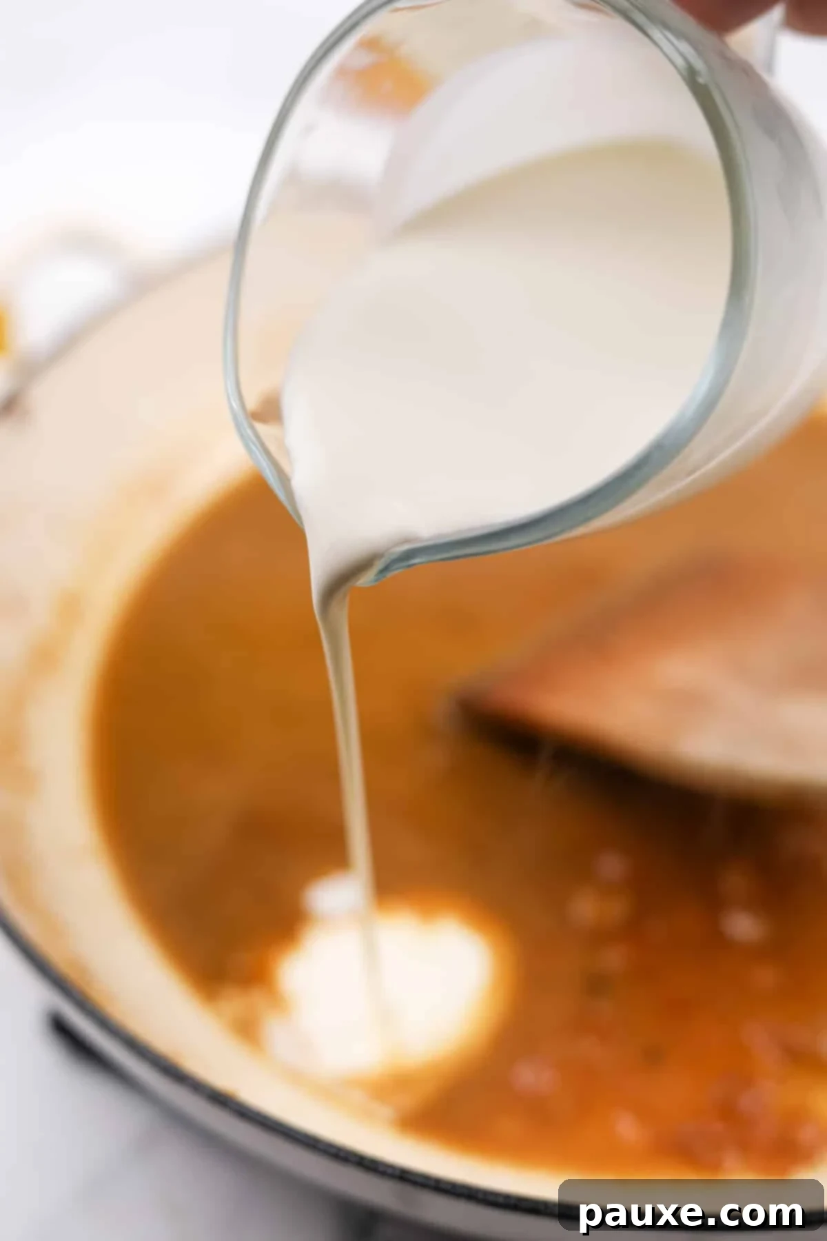Rich heavy cream being poured into the skillet with the deglazed broth and aromatics, to create the creamy sauce.