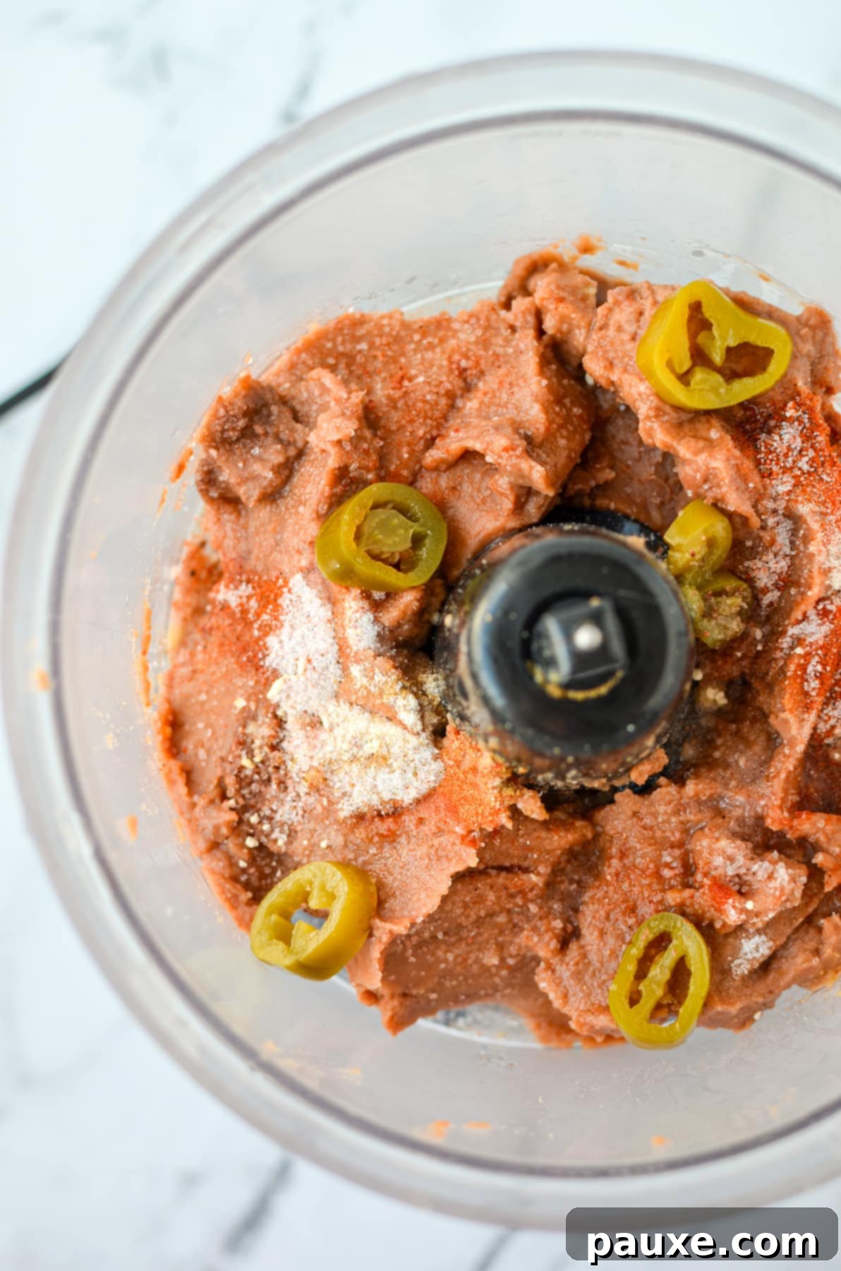 Craveable Homemade Fritos Bean Dip 4 A food processor with refried beans, jalapeno slices, and seasonings.