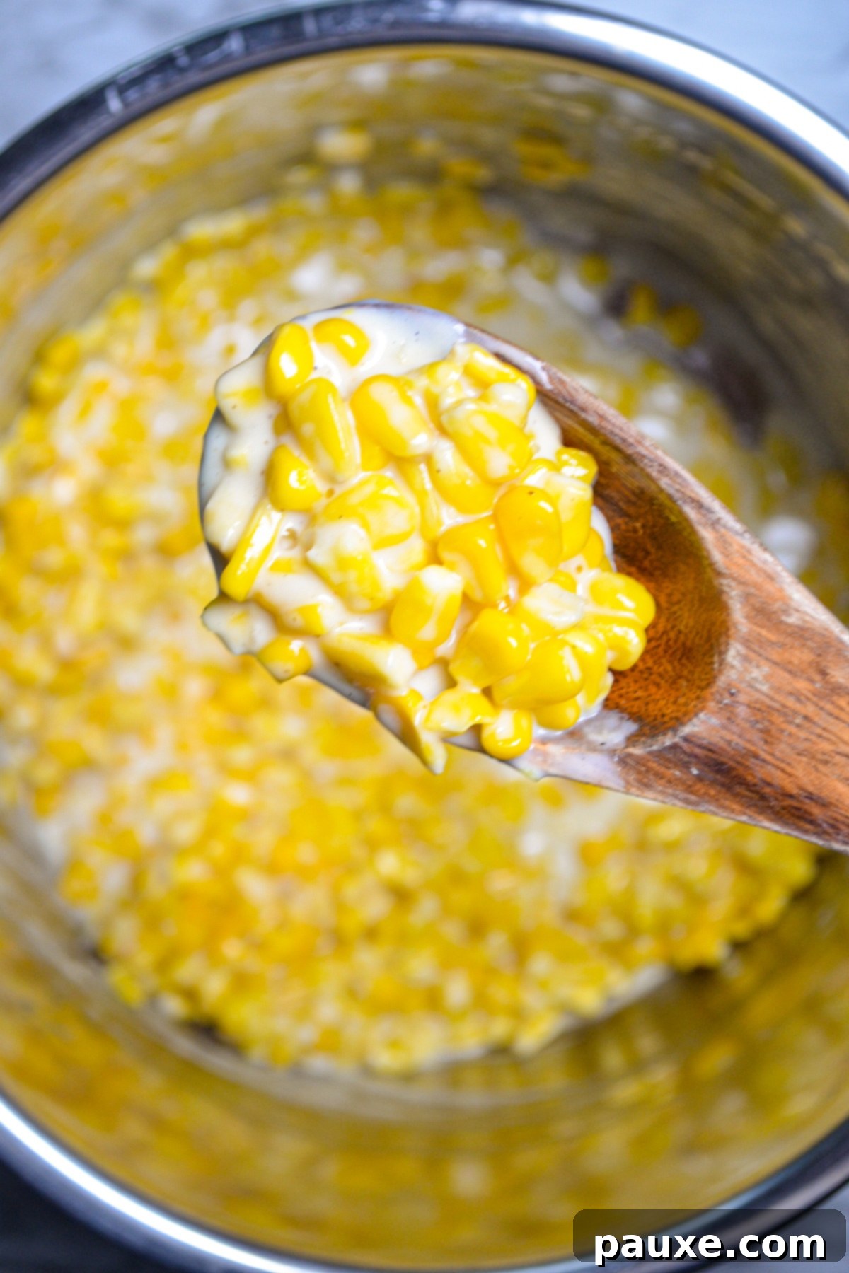 An Instant Pot filled with creamed corn; a wooden spoon lifting a portion from the pot.
