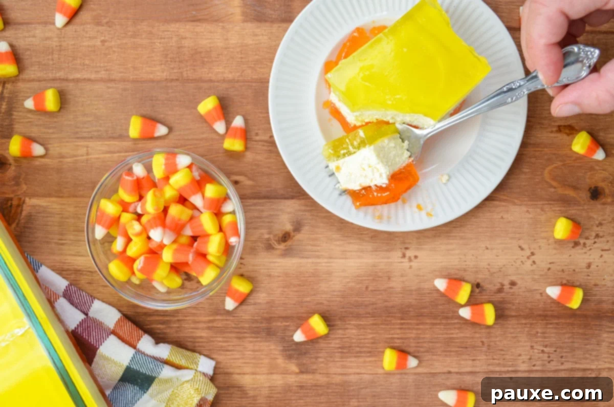 Spooky Layered Gelatin 3 A fork cuts into a slice of layered lemon and orange jello dessert, with a bowl of colorful candy corn nearby.