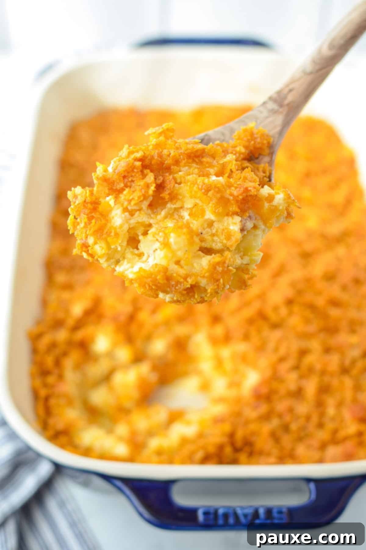 Effortless Cheesy Funeral Potatoes 8 A wooden spoon taking a portion of party potatoes.