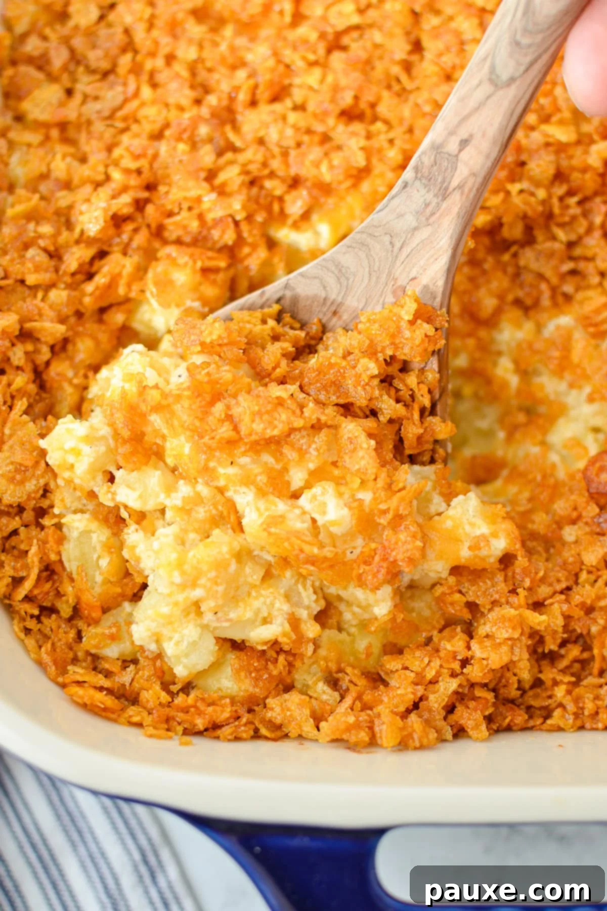 Effortless Cheesy Funeral Potatoes 9 Scooping a portion of hash brown casserole from a baking dish.