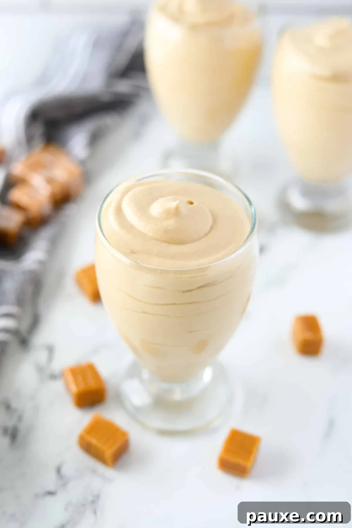 Decadent Dulce De Leche Cloud 6 A single jar of decadent dulce de leche mousse, perfectly set, is surrounded by a scattering of unwrapped caramels, emphasizing its rich flavor.