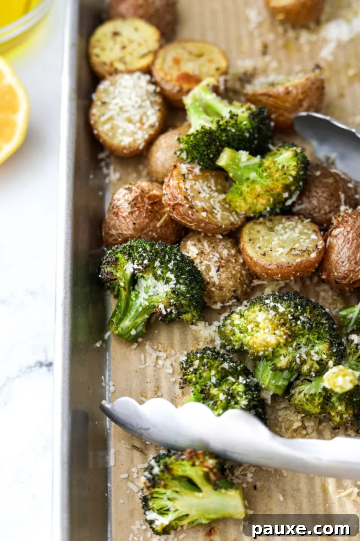 Golden Roasted Broccoli and Potatoes 2 Tongs picking up roasted broccoli and potatoes from a sheet pan.