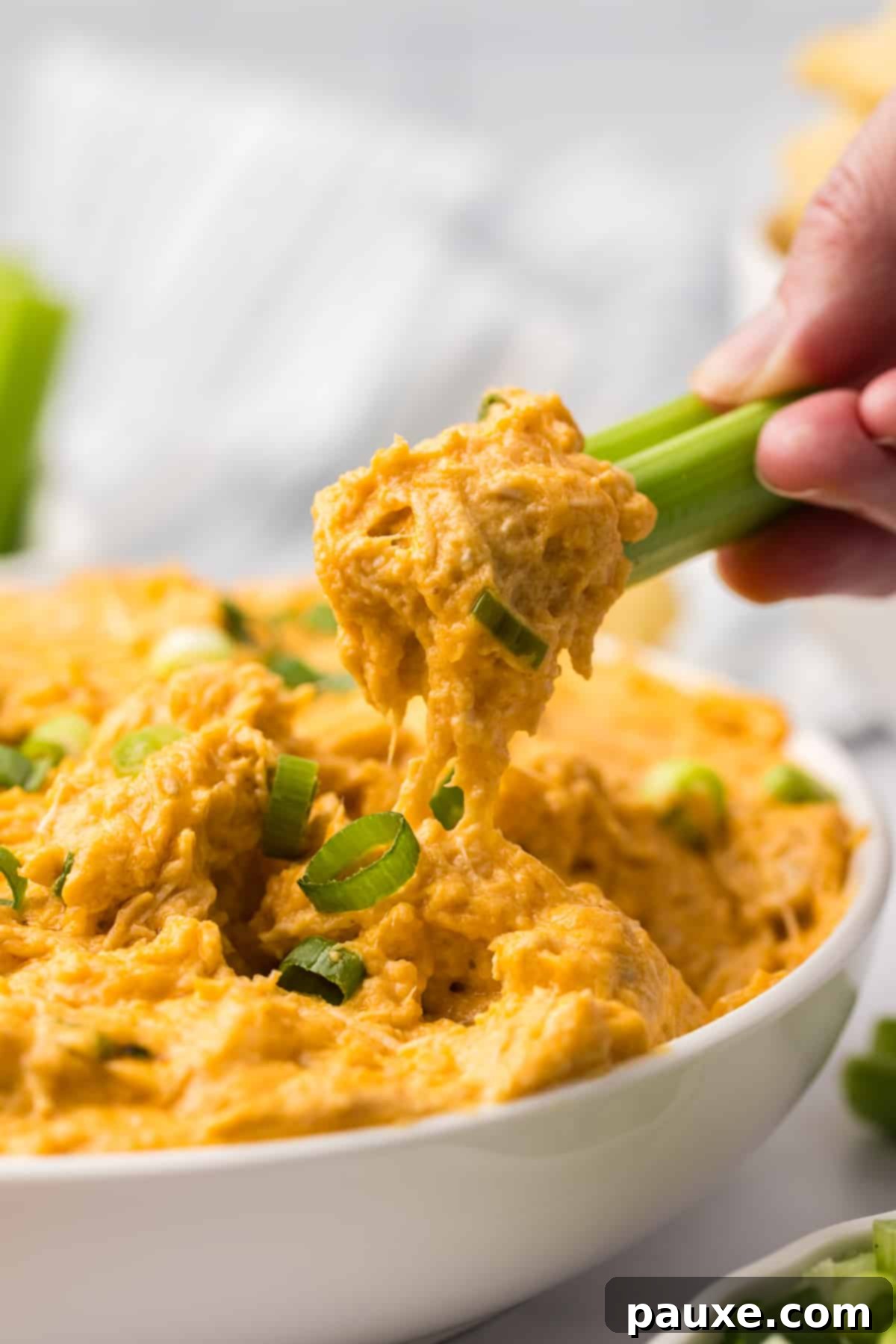 Zesty Slow Cooker Buffalo Chicken Dip 11 A fresh celery stick being dipped into a bowl of warm buffalo chicken dip, highlighting its creamy texture.