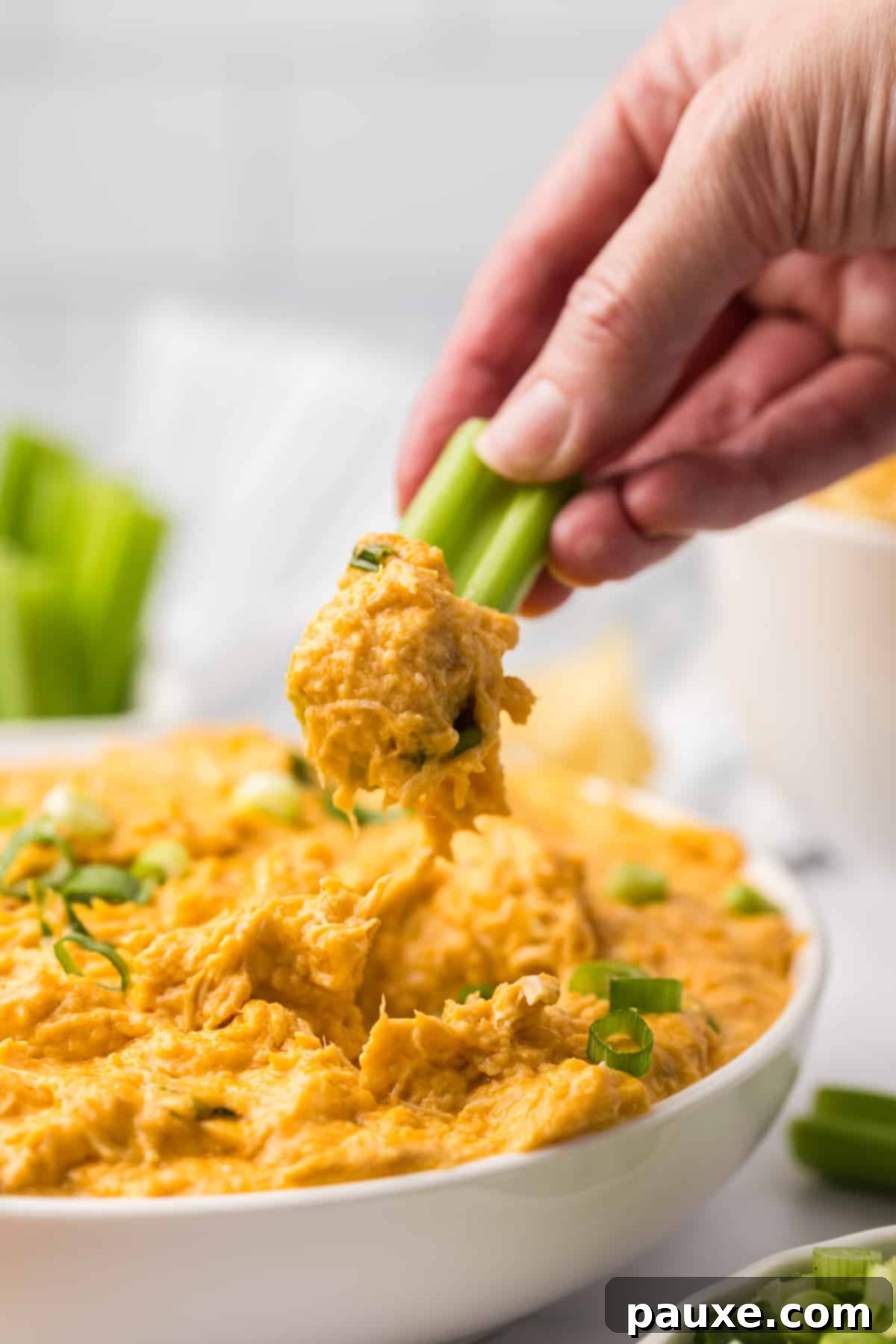 Zesty Slow Cooker Buffalo Chicken Dip 15 A hand dipping a fresh celery stick into a bowl of warm, inviting buffalo chicken dip, highlighting its creamy texture and deliciousness.