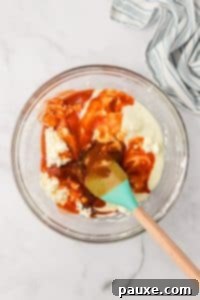 Zesty Slow Cooker Buffalo Chicken Dip 18 A glass bowl filled with a cream cheese mixture, with cayenne pepper sauce inside.