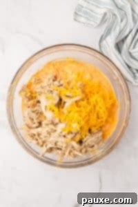 Zesty Slow Cooker Buffalo Chicken Dip 19 A bowl filled with a dip mixture, with shredded cheese and cooked chicken on top.