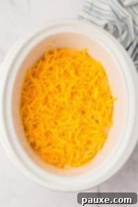 Zesty Slow Cooker Buffalo Chicken Dip 21 A white crock pot with a cheesy dip inside, topped with shredded cheddar cheese.