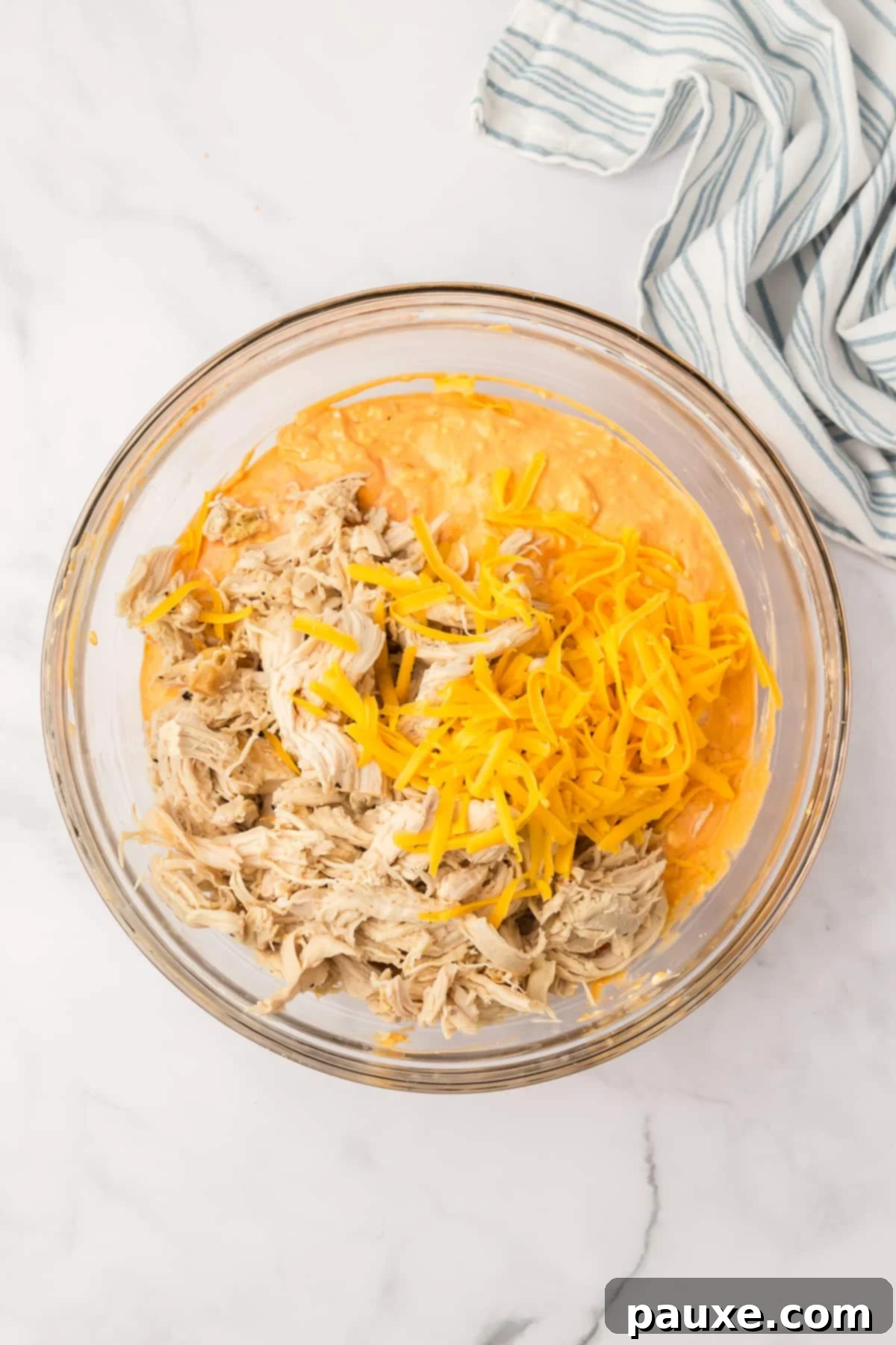 Zesty Slow Cooker Buffalo Chicken Dip 7 A bowl filled with the dip mixture, now with shredded cheddar cheese and cooked shredded chicken added on top, ready to be mixed.