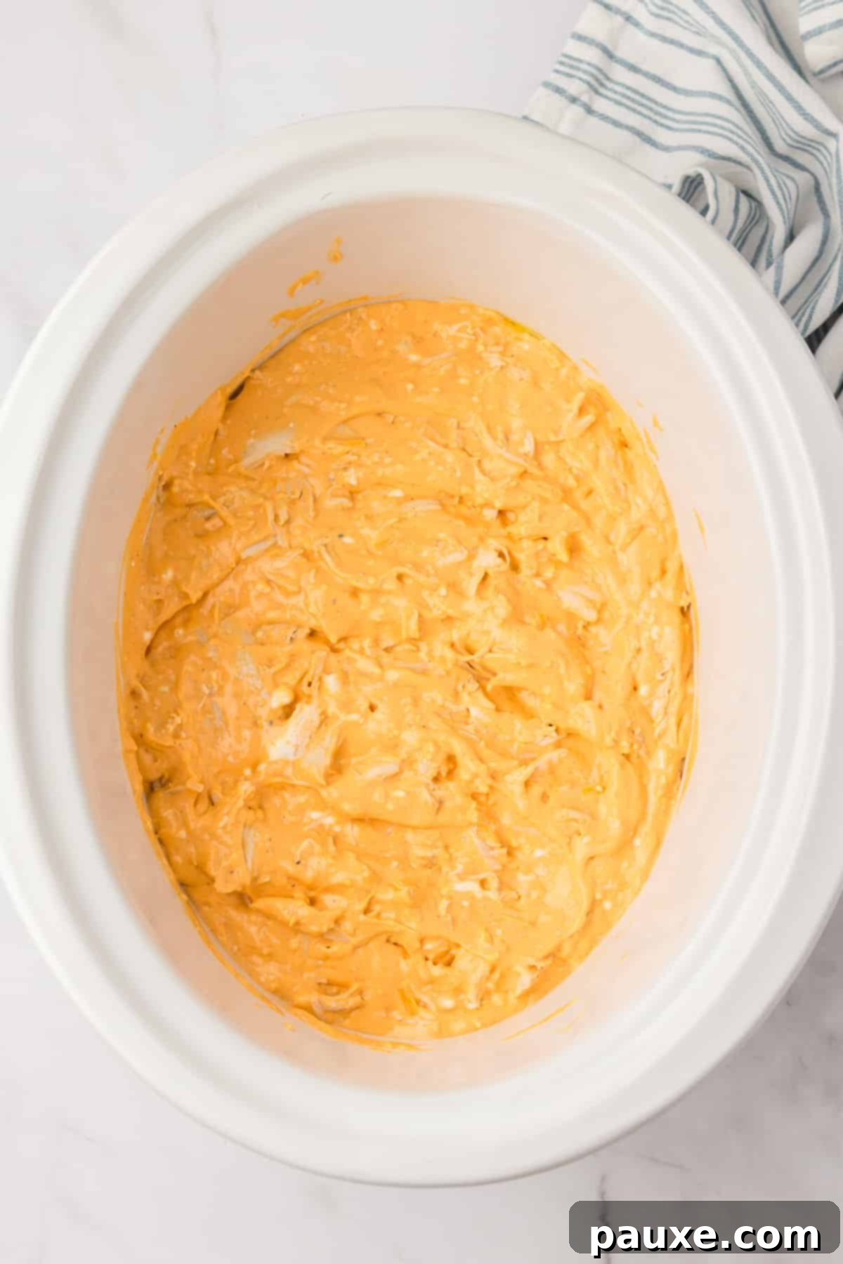 Zesty Slow Cooker Buffalo Chicken Dip 8 A white slow cooker insert filled with the unbaked cheesy chicken dip mixture, spread evenly.
