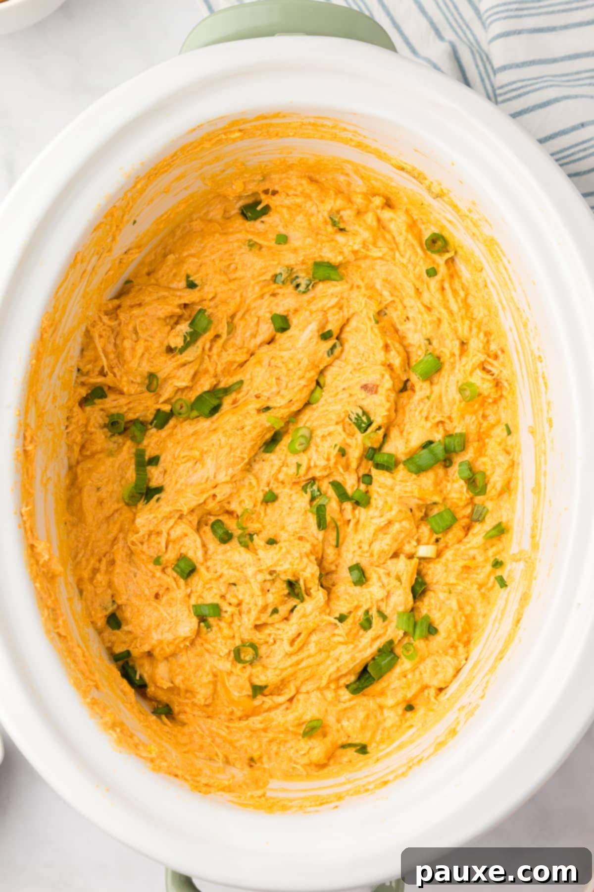 Zesty Slow Cooker Buffalo Chicken Dip 10 A white crock pot showcasing the finished, hot, and bubbly cheesy chicken dip, ready to be served.