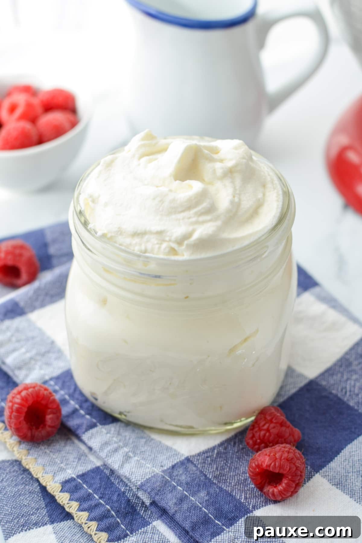 A jar of homemade whipped cream, surrounded by raspberries.