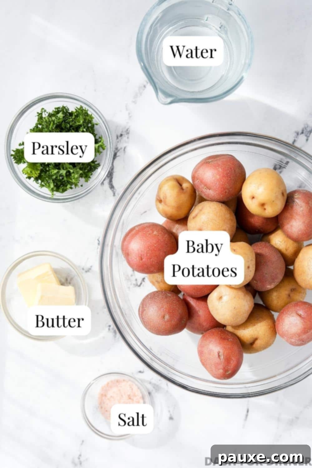 Perfect Instant Pot Baby Potatoes 3 A flat lay photograph showcasing the simple ingredients for Instant Pot Baby Potatoes: a bowl of fresh baby potatoes, a dish of butter, a small pile of salt, a sprig of parsley, and a glass of water.