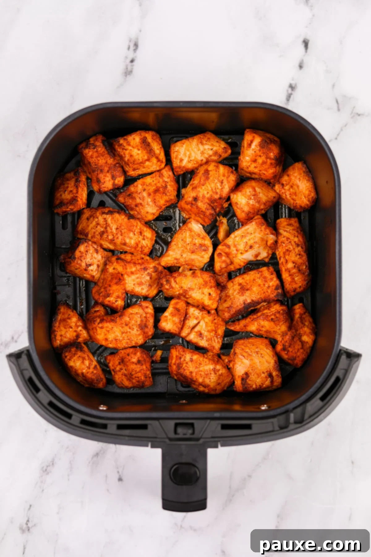 Air-Fried Salmon Nuggets 7 An air fryer basket with perfectly cooked and browned salmon pieces, ready to serve.