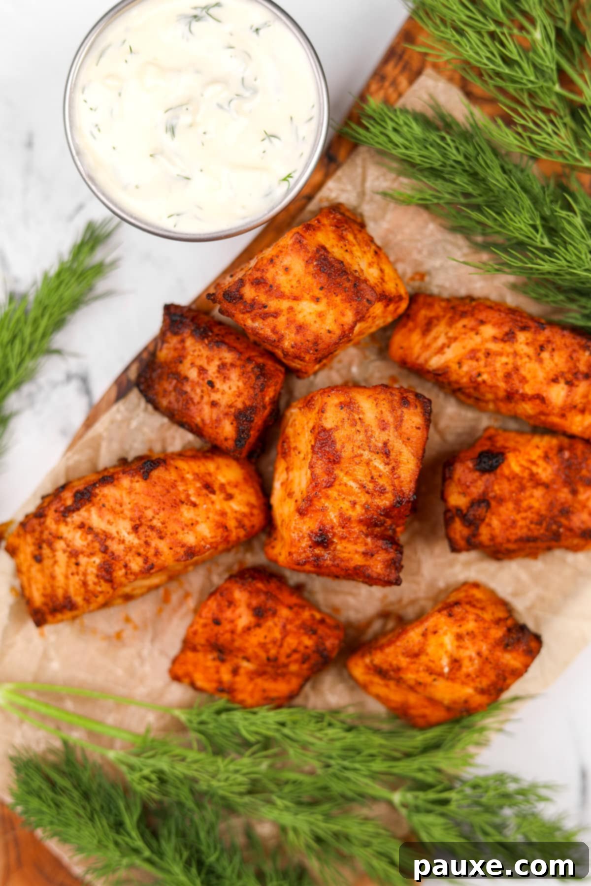 Air-Fried Salmon Nuggets 9 A close-up shot of cooked salmon bites next to a small dish of creamy dill sauce, ready for dipping.