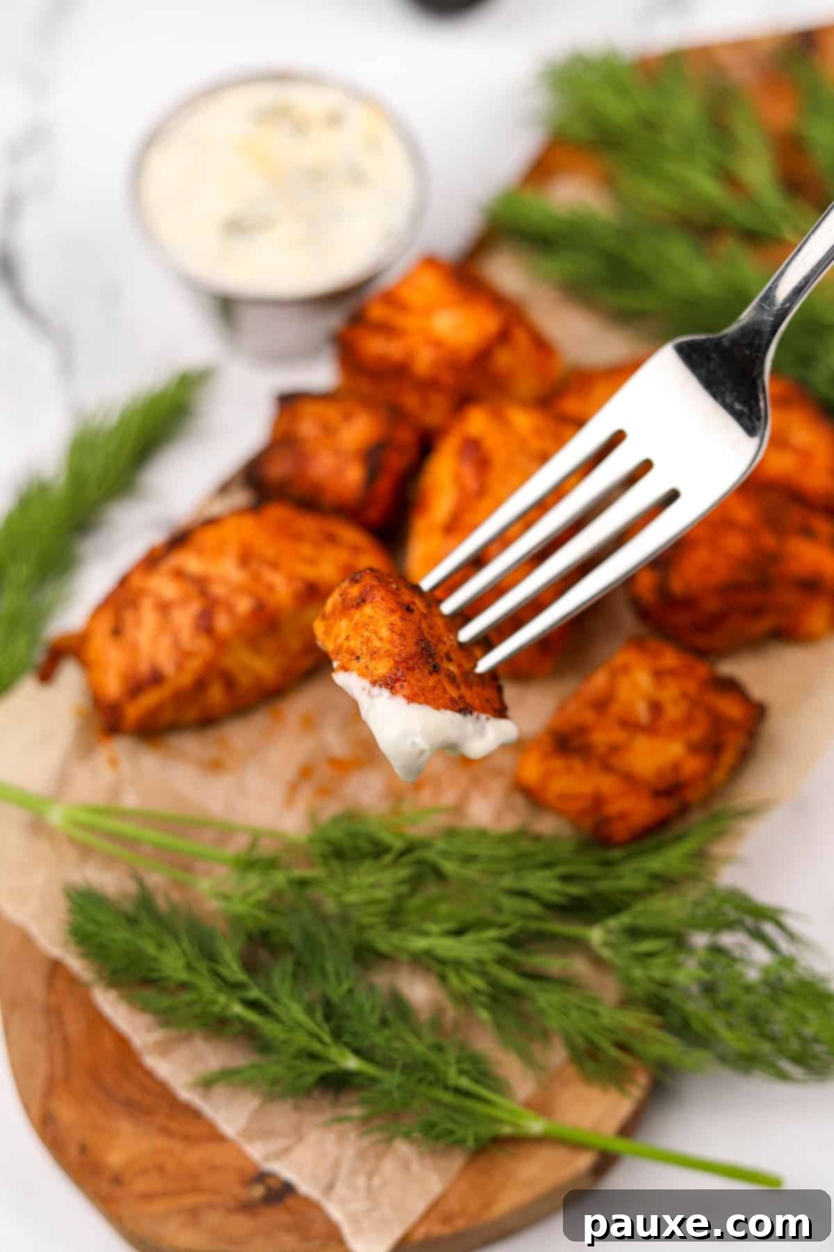 Air-Fried Salmon Nuggets 10 A hand dipping a crispy air fryer salmon bite into a small bowl of creamy sauce.