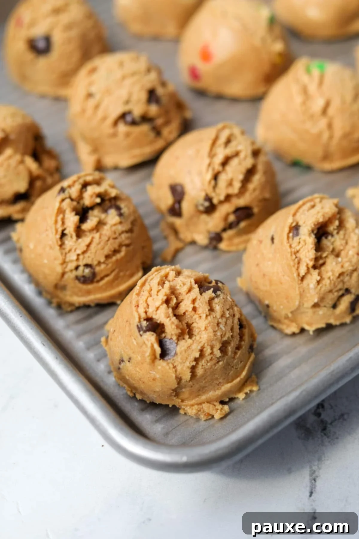 Guilt-Free Protein Cookie Dough 2 Scoops of healthy protein cookie dough artfully arranged on a minimalist baking sheet, ready for chilling or serving. The texture and mix-ins are clearly visible, promising a delicious and satisfying treat.