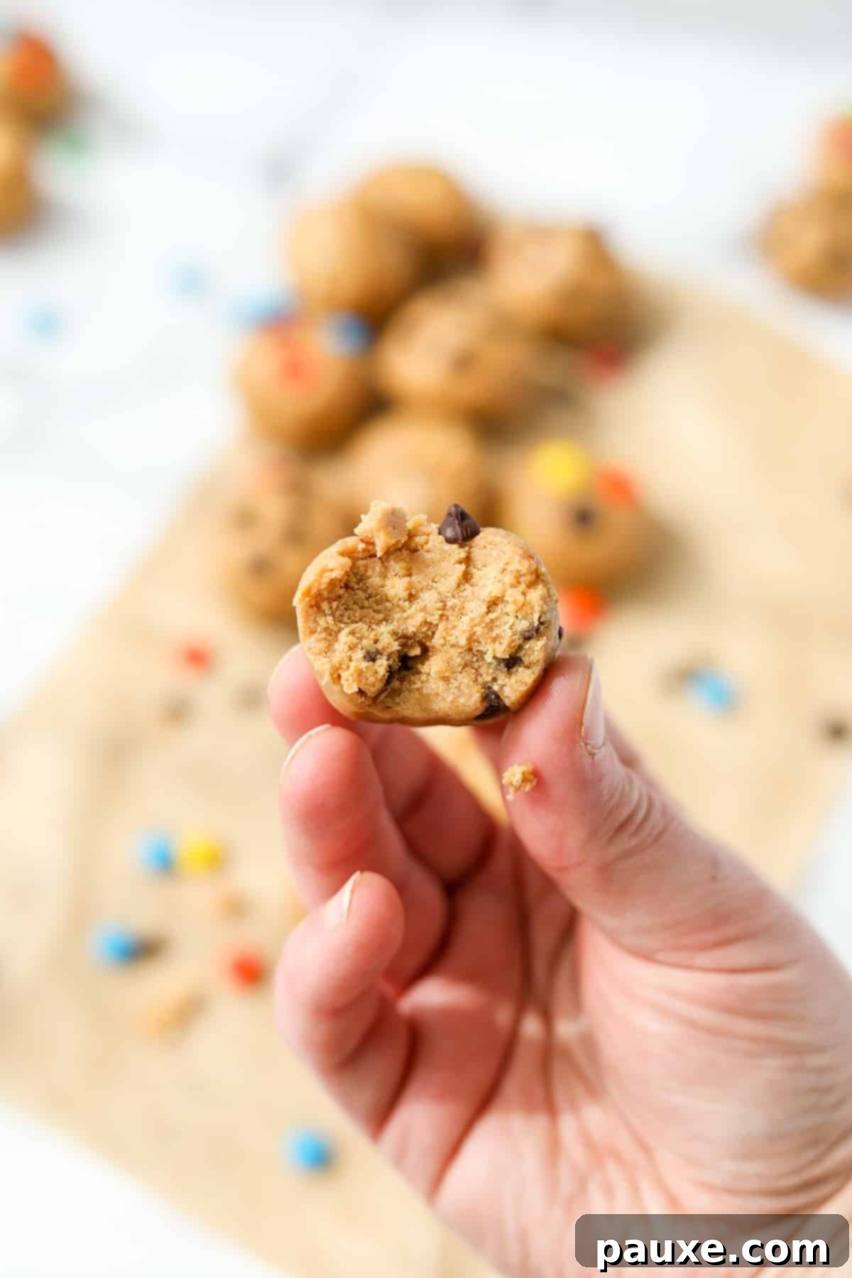 Protein-Packed Cookie Dough Bites 12 A hand holding up a protein cookie dough ball with a bite taken out of it, showing the inside texture and mix-ins.