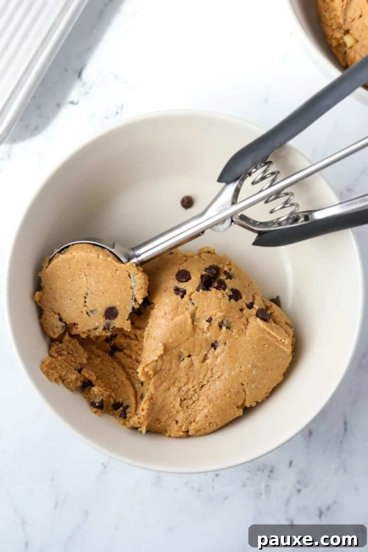 Protein-Packed Cookie Dough Bites 8 A bowl with protein cookie dough being scooped by a cookie scoop, demonstrating portioning.