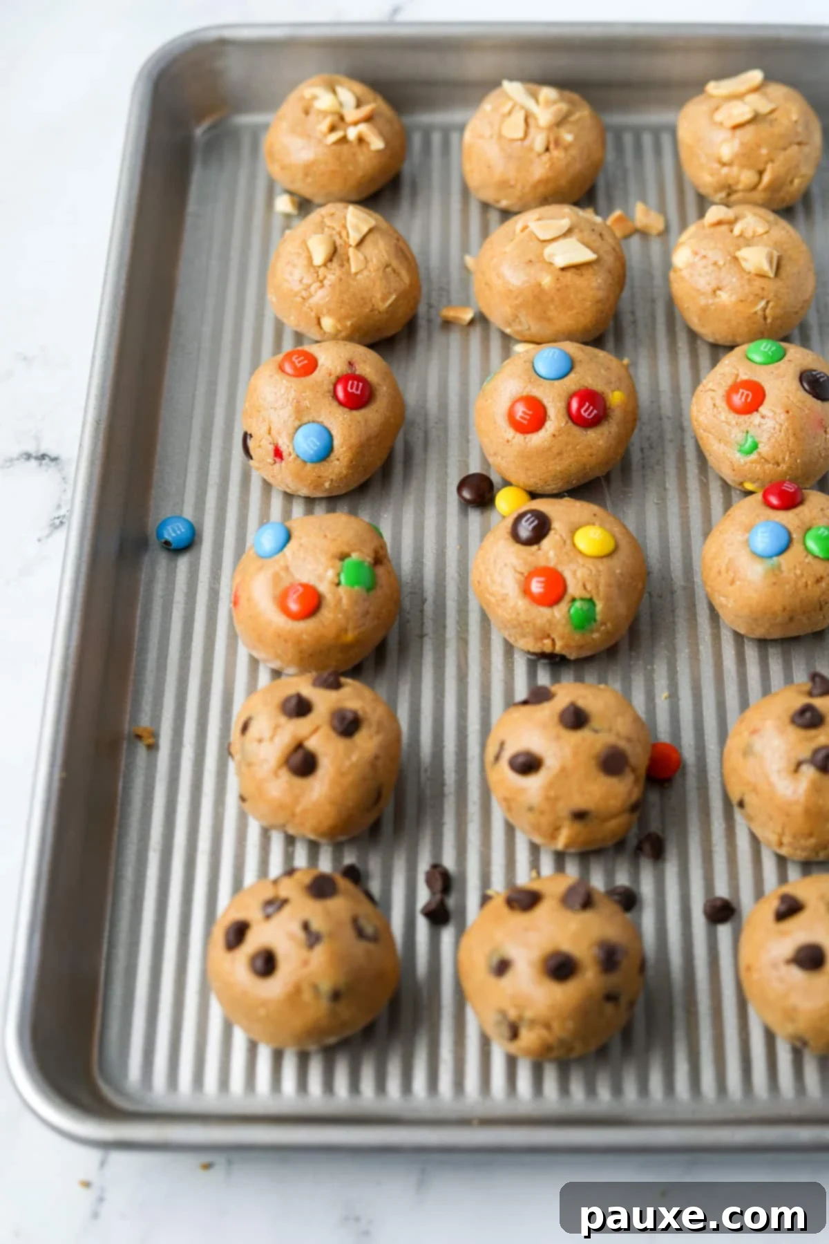 Protein-Packed Cookie Dough Bites 10 A baking tray with cookie dough balls, featuring chocolate chip, M&M, and chopped peanuts, ready for chilling.