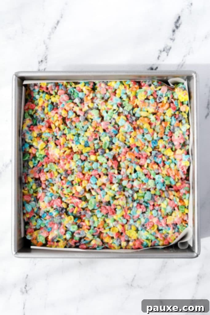 Colorful Pebbles Bars 7 A baking pan, lined with parchment paper, filled with the colorful Fruity Pebbles cereal treat mixture, smoothed into an even layer.