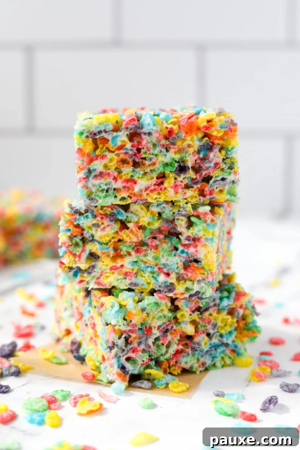 Colorful Pebbles Bars 9 A stack of three neatly cut Fruity Pebbles cereal treats on a white tile background, highlighting their uniform size and colorful texture.