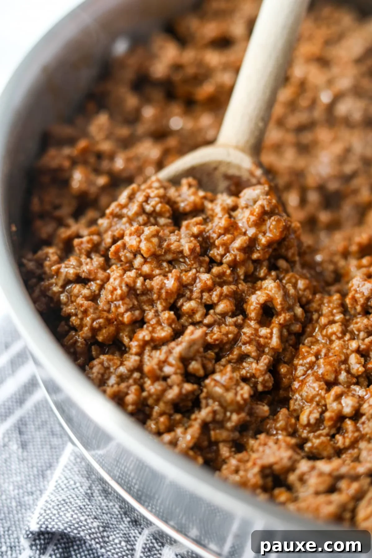 A wooden spoon scooping seasoned ground beef taco meat from a hot skillet.