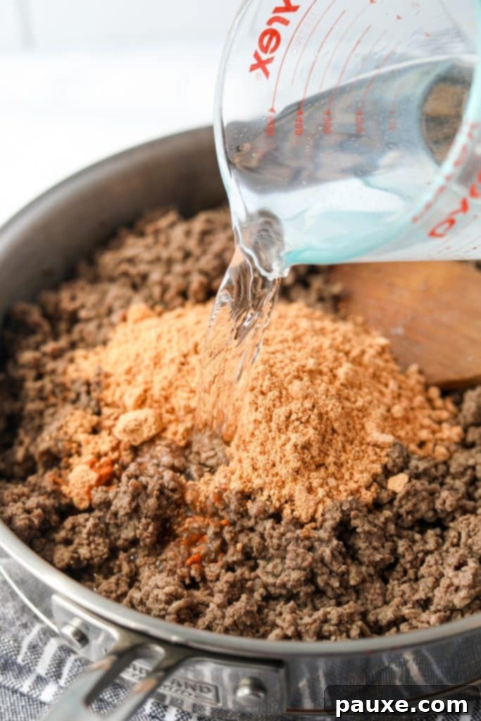 Taco seasoning and water being added to cooked ground beef in a skillet.