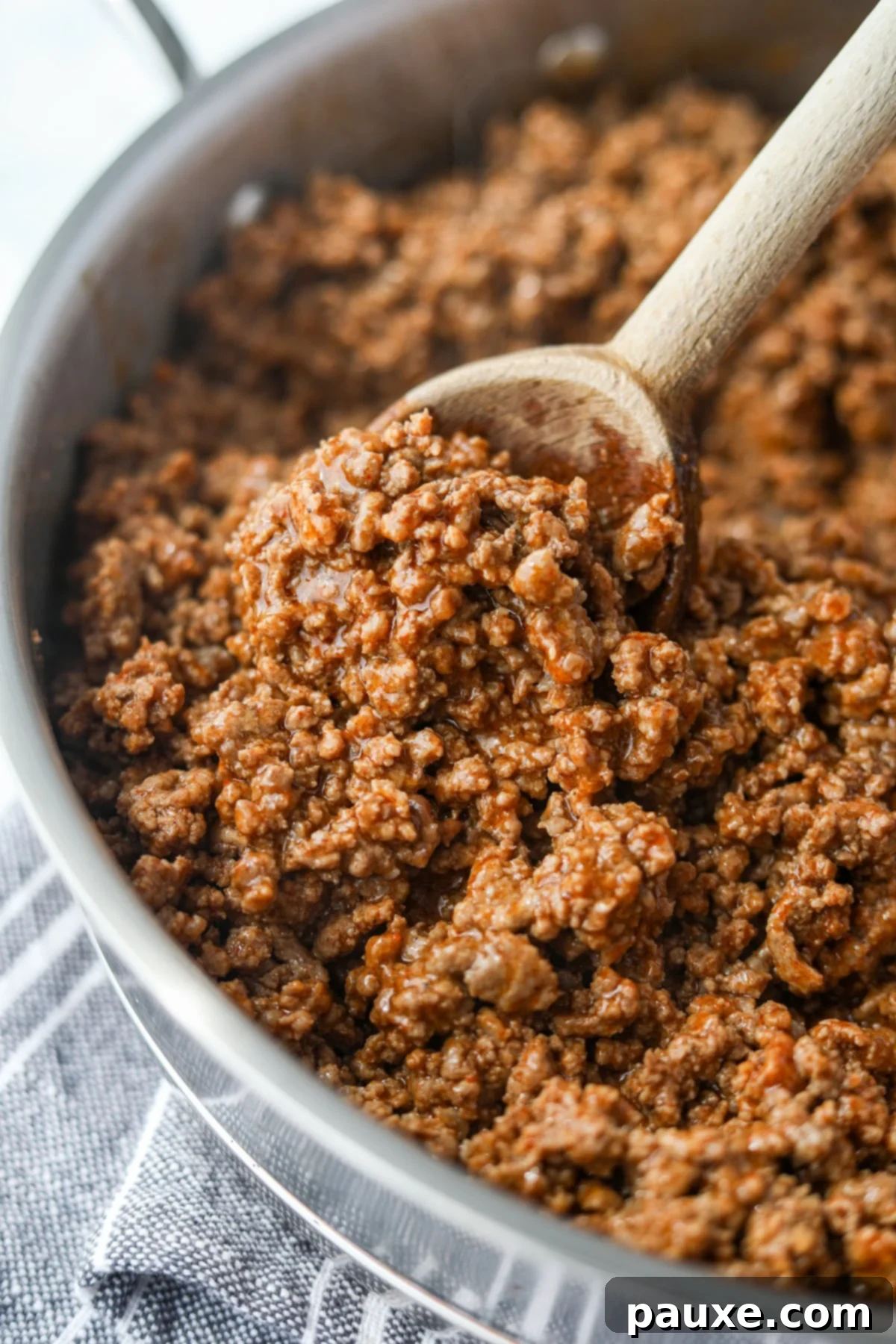 A wooden spoon stirring cooked ground beef in a skillet.