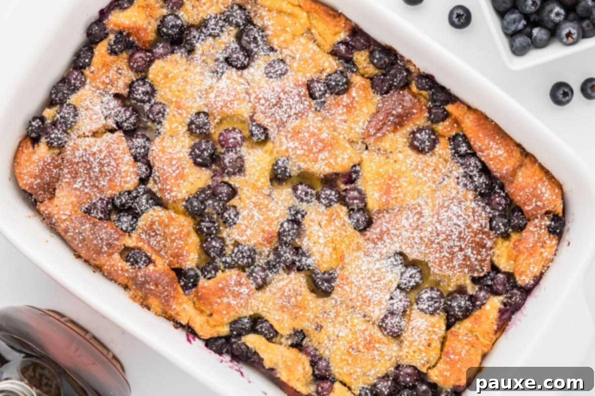 Overnight Brioche French Toast Bake 12 A large rectangular French toast casserole, garnished generously with fresh blueberries and a dusting of powdered sugar, presented beautifully in its baking dish.