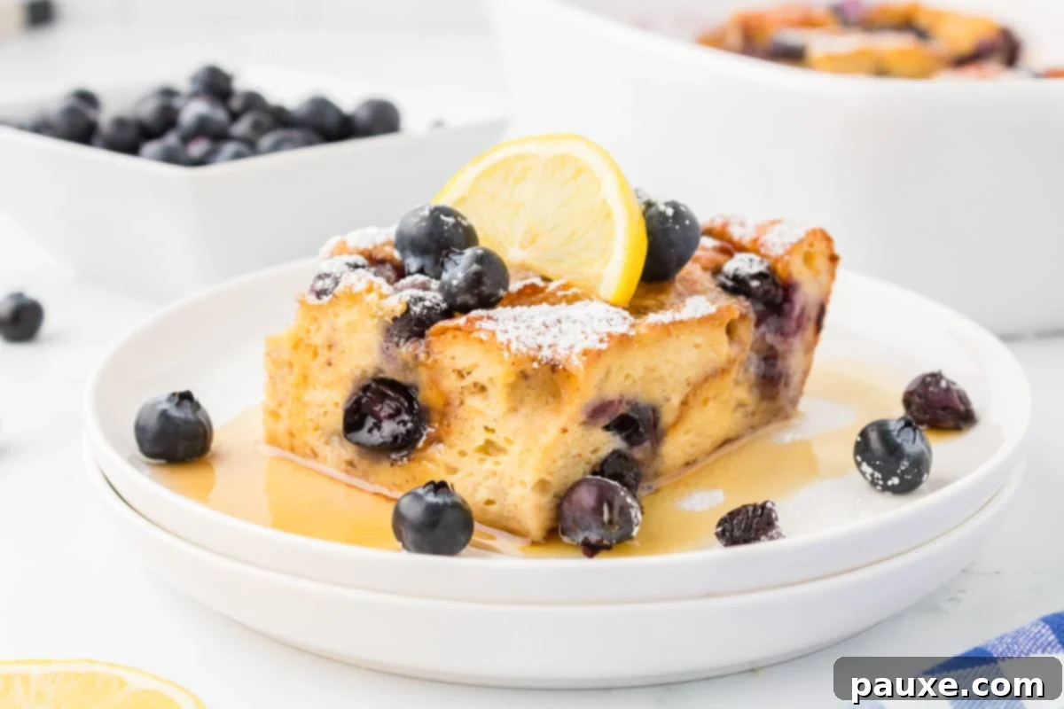 Overnight Brioche French Toast Bake 16 A square serving of baked French toast casserole, garnished with fresh lemon slices and blueberries, on a white plate.