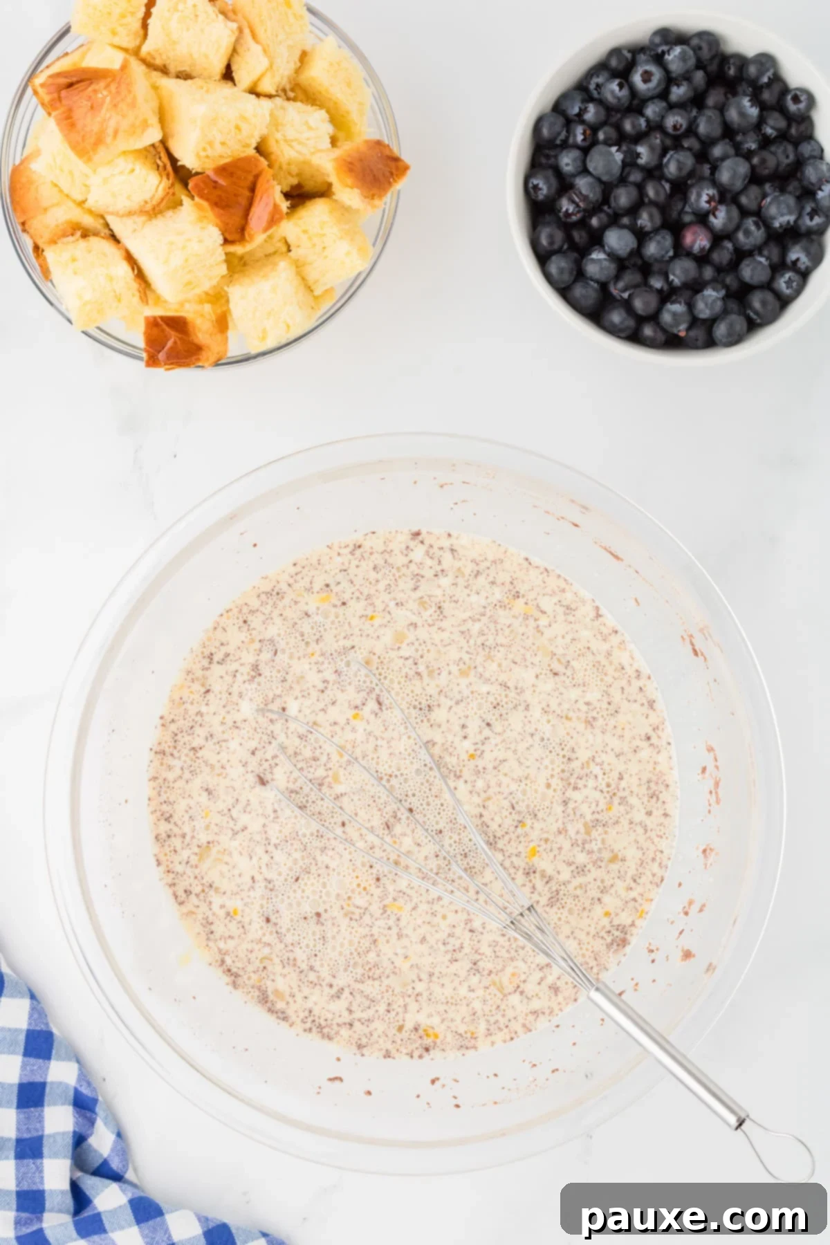 Overnight Brioche French Toast Bake 5 A creamy, pale yellow custard mixture in a large mixing bowl, thoroughly whisked and ready for the bread, with flecks of cinnamon visible.