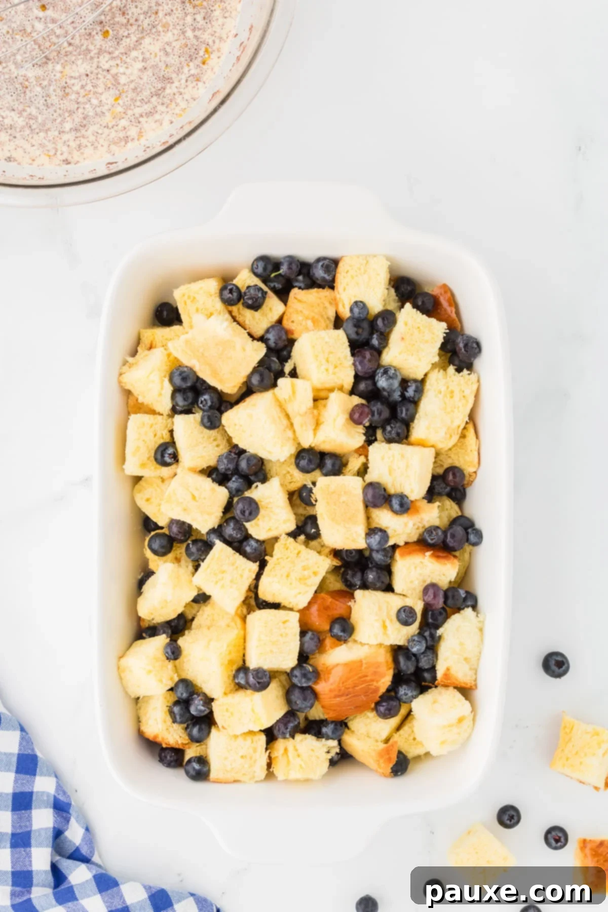 Overnight Brioche French Toast Bake 7 A baking dish filled with two layers of brioche bread cubes interspersed with fresh blueberries, showcasing the alternating layers before the custard is added.