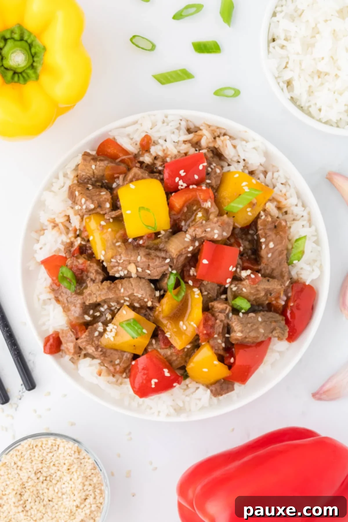 Easy Slow Cooker Pepper Steak 2 An overhead view of a bowl of pepper steak served over rice, garnished with sesame seeds and green onions.