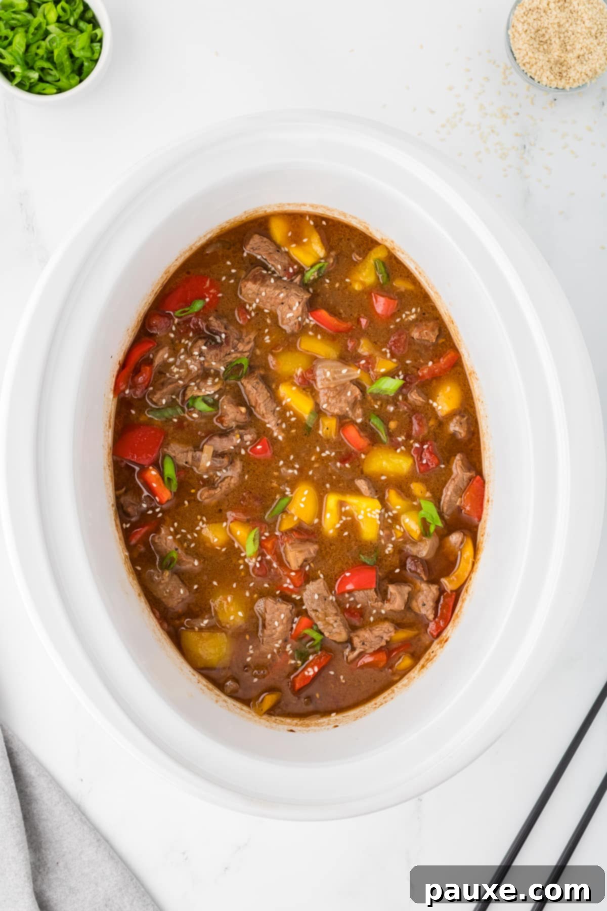 Easy Slow Cooker Pepper Steak 11 A slow cooker filled with a saucy pepper steak, fully cooked and garnished with sesame seeds and green onions.