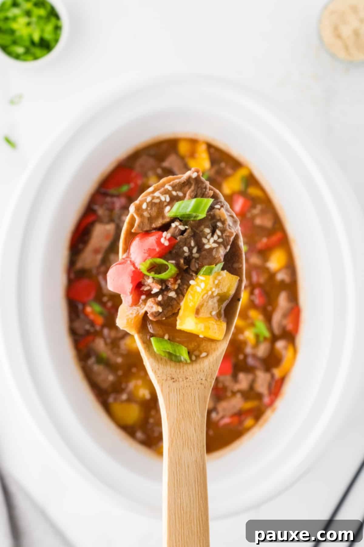 Easy Slow Cooker Pepper Steak 12 A wooden spoon taking a portion of pepper steak from a crock pot, showcasing its rich sauce and tender ingredients.