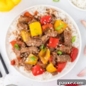Easy Slow Cooker Pepper Steak 16 An overhead view of a bowl of pepper steak served with rice and garnished with sesame seeds.