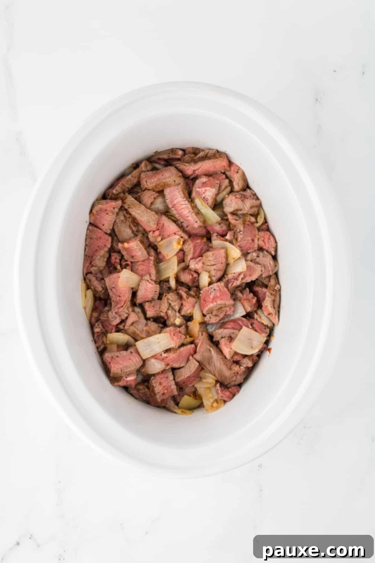 Easy Slow Cooker Pepper Steak 7 A slow cooker with browned beef, onions, and garlic added to the bottom.