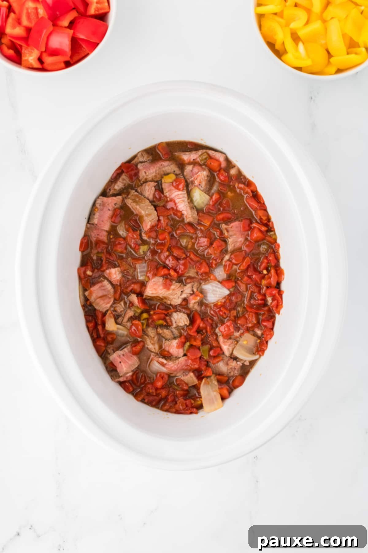 Easy Slow Cooker Pepper Steak 9 An overhead view of a crock pot filled with sauce, meat, and onions, ready for cooking.