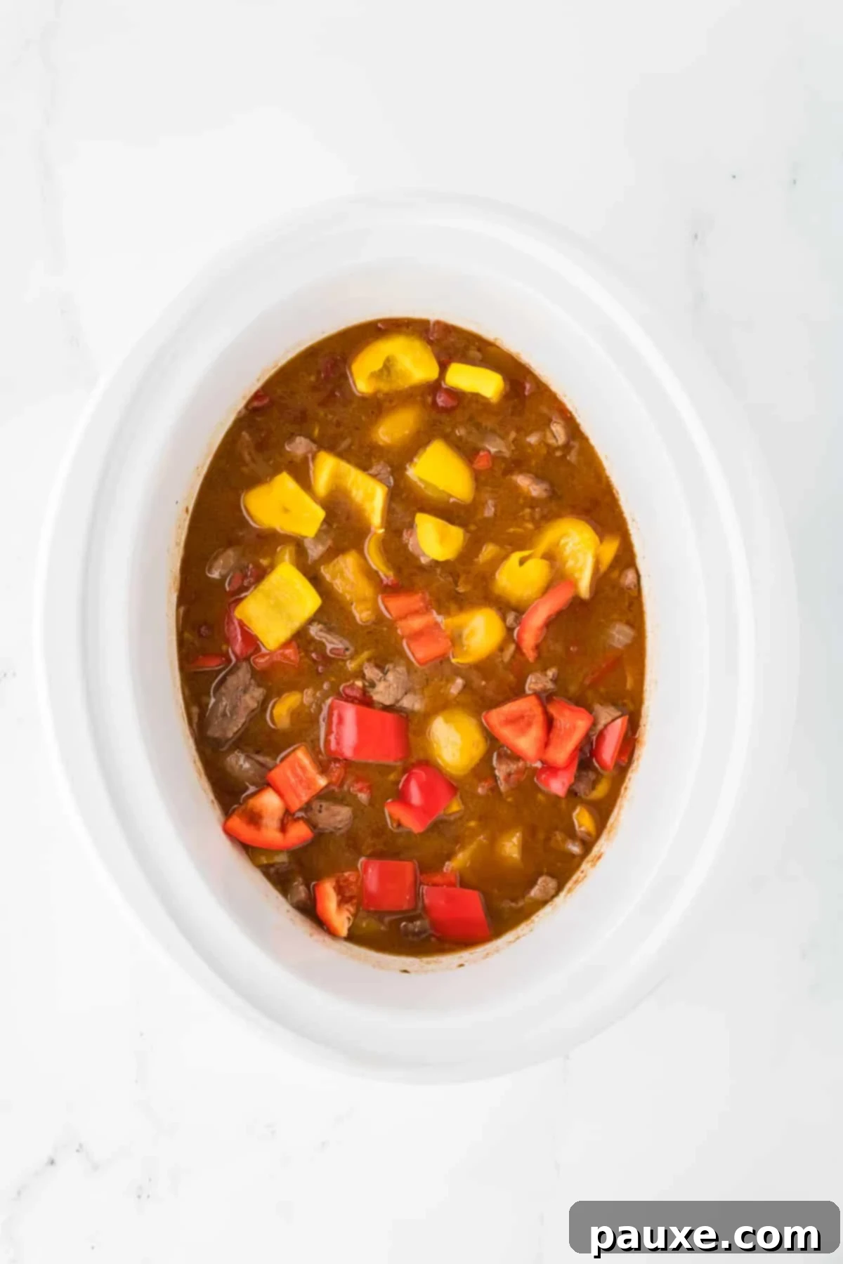 Easy Slow Cooker Pepper Steak 10 A slow cooker filled with sauce, meat, and freshly added bell peppers, ready to finish cooking.