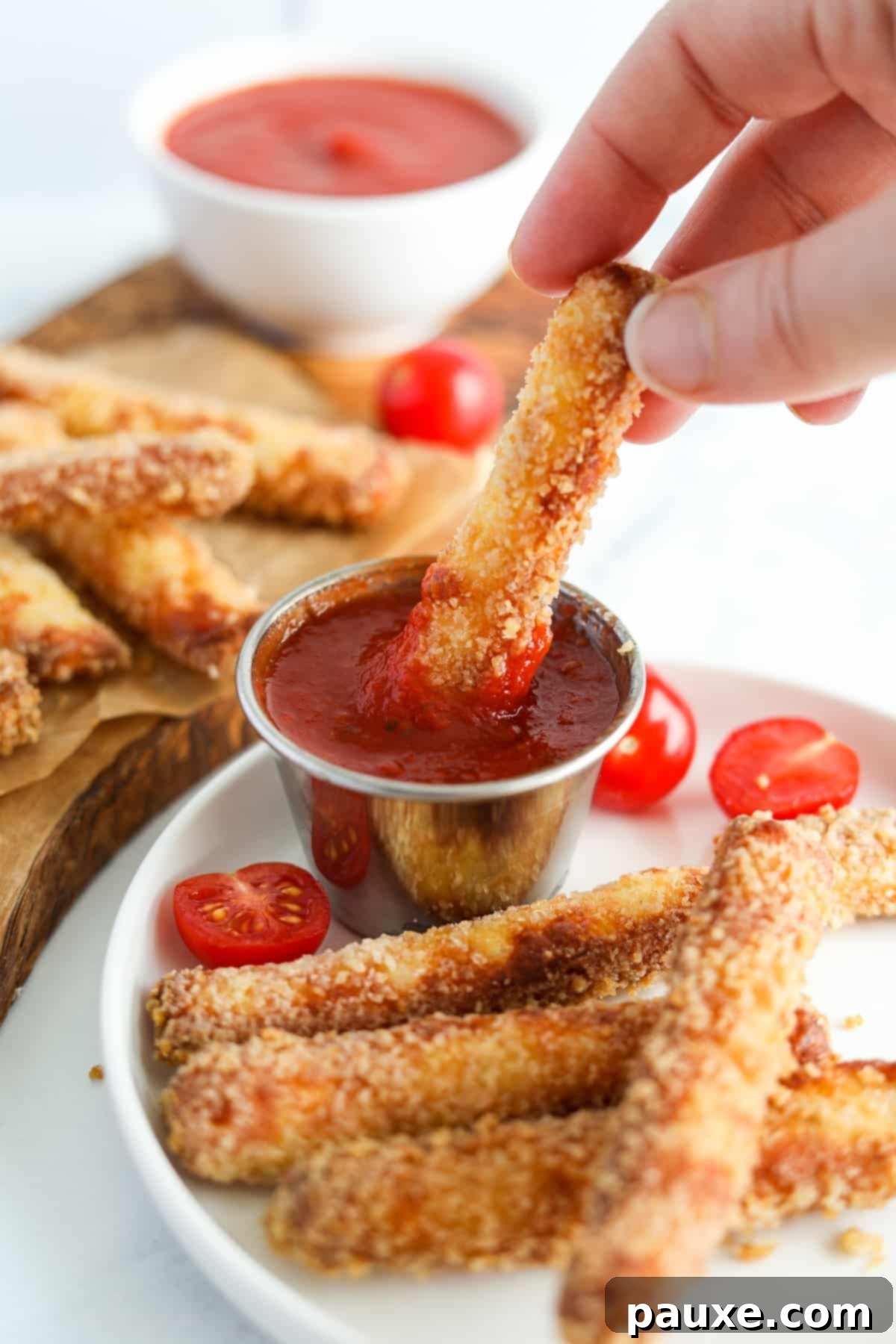 Crispy Air Fryer Halloumi Fries 11 A hand dipping a golden, crispy air fryer halloumi fry into a small bowl of rich marinara sauce, showcasing its perfect texture.