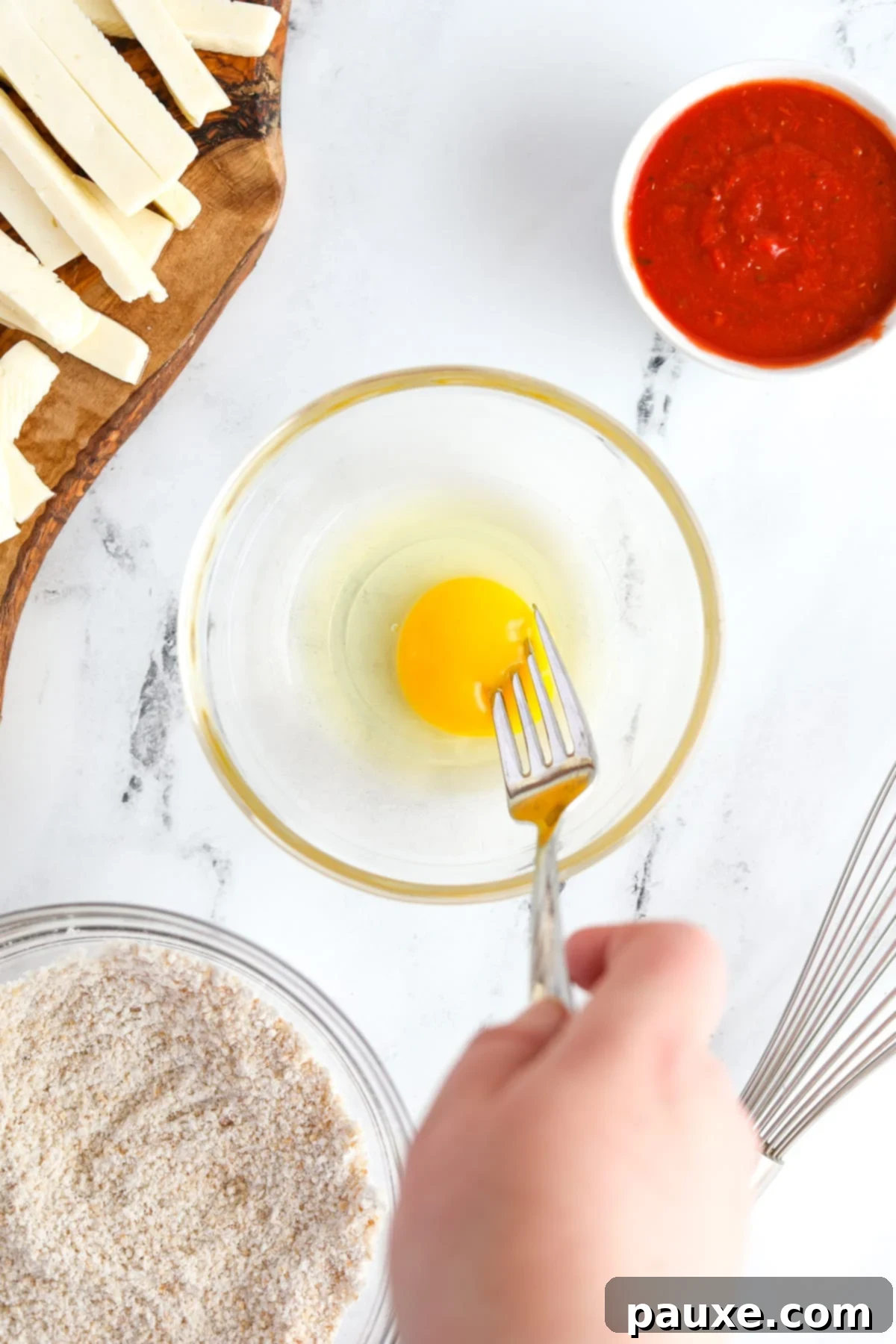 Crispy Air Fryer Halloumi Fries 6 A small, shallow dish holding a single large egg, being vigorously whisked with a fork until the yolk and white are fully incorporated.