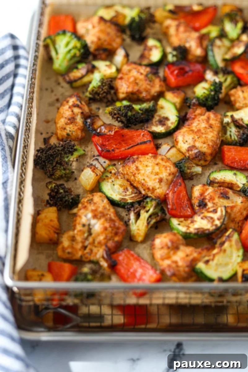 Crispy Air Fryer Chicken and Veggies 11 An air fryer tray lined with parchment paper, showcasing golden-brown cooked chicken pieces and a colorful assortment of vegetables.